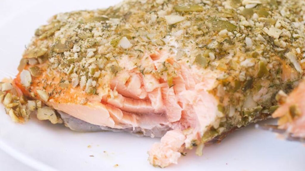 A salmon filet crusted with pumpkin seeds. A bit is taken from the filet.