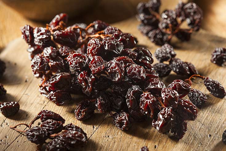 A bunch of raisins on a cutting board.