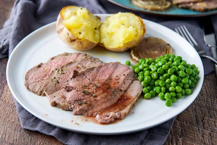 A plate with roast beef, a baked potato and some peas.