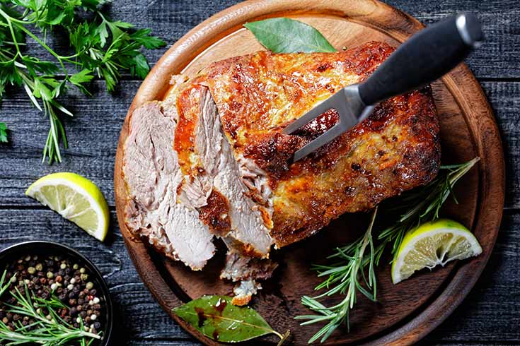 An overhead view of a pork roast with some slices cut and a fork sticking in the middle of the roast.