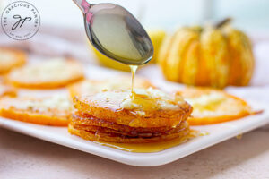 A spoon drizzles some syrup over slices of squash on a platter.