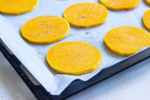 Slices of butternut squash laying on a parchment-lined baking sheet.