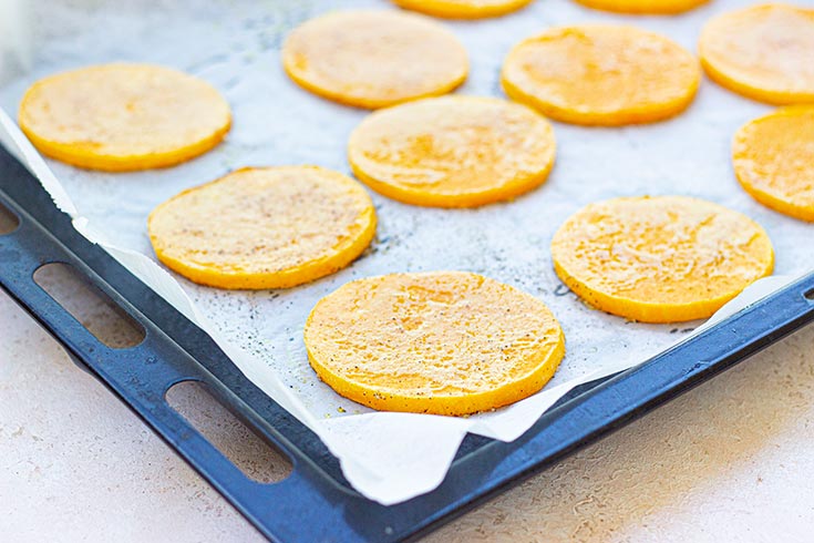 Slices of squash on a baking pan drizzled with oil.