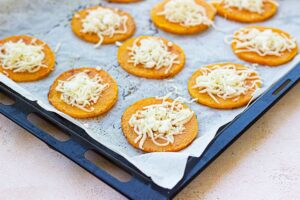 Grated cheese sprinkled on top of squash slices on a baking sheet.