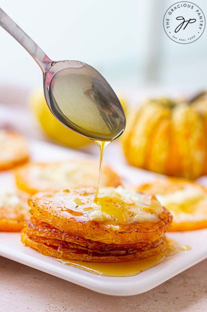 A spoon drizzling syrup over some cheesy squash slices.
