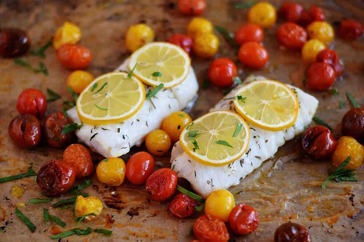 Two cod filets on parchment surrounded by roasted grape tomatoes.