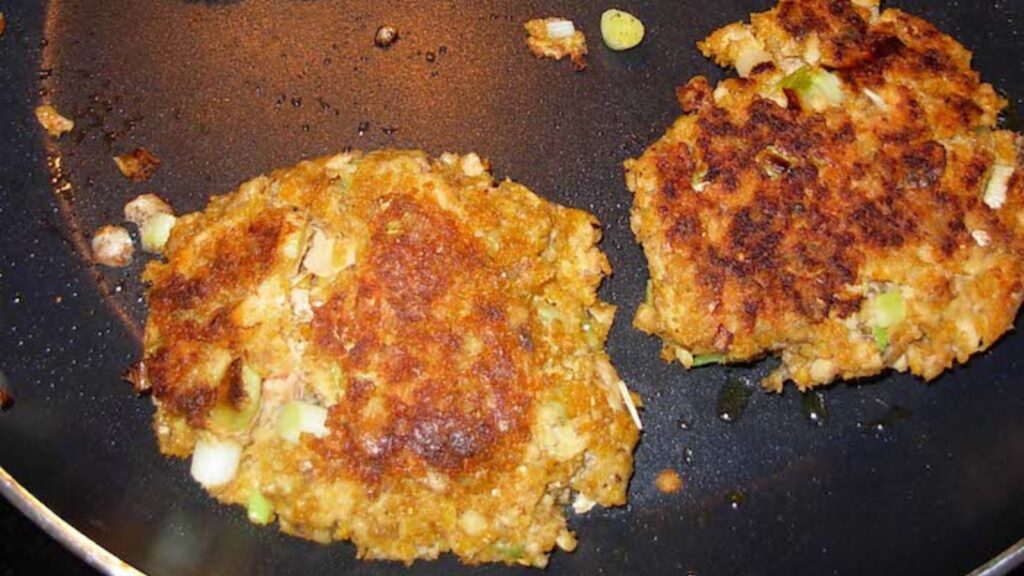 Two salmon patties cooking in a skillet.