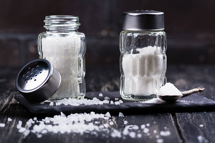 Glass salt shakers with sea salt coarse and fine on dark wooden table.