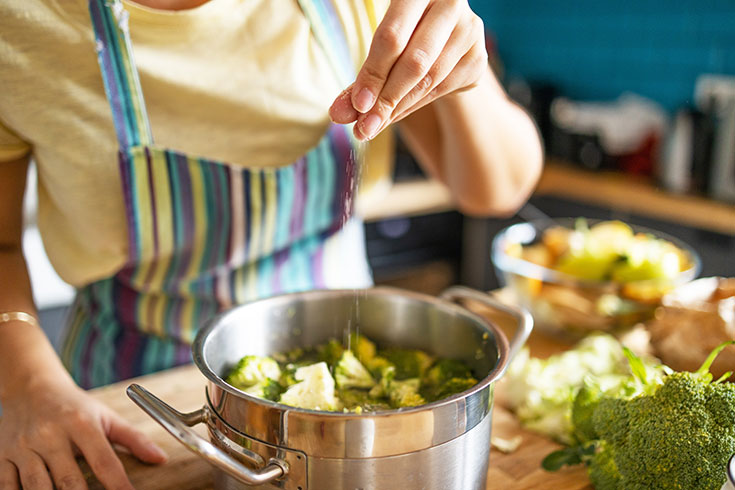 A woman seasoning a pot of chopped vegetables in a pot.