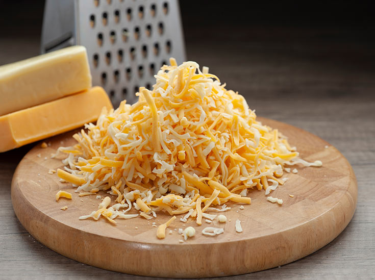 A round cutting board with a pile of grated cheese on it.