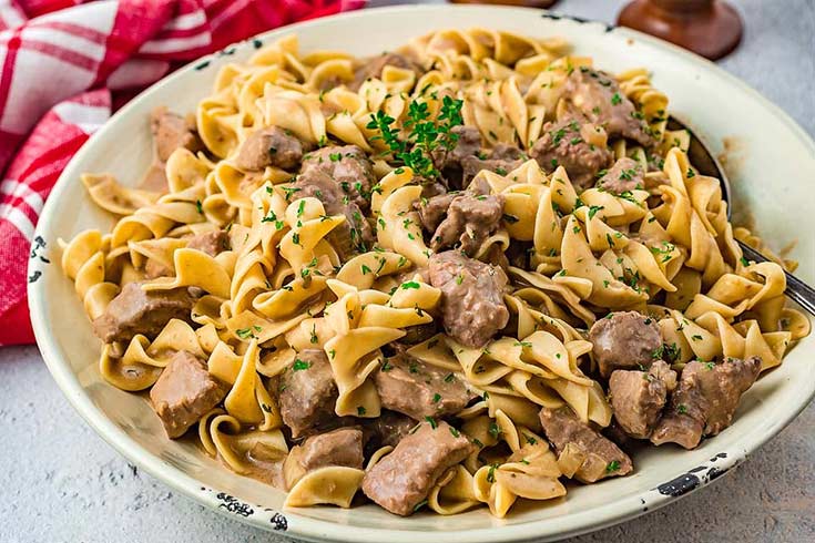 A white bowl on a table filled with slow cooker beef and noodles with mushrooms.