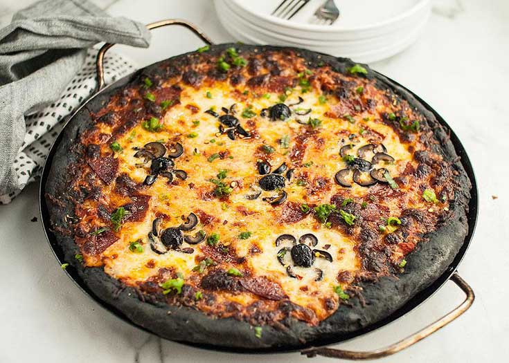 A pizza with black crust and black olive spiders on top.