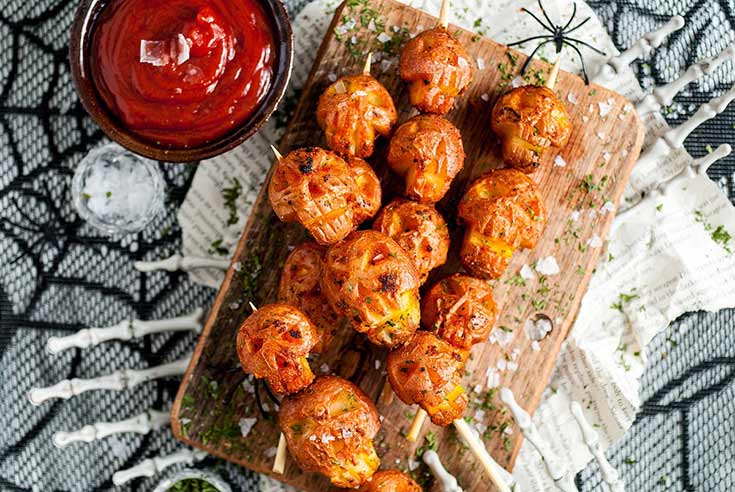 An overhead view of skull-shaped potatoes on skewers laying on a cutting board.