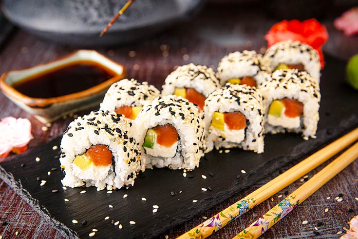 Sushi rolls cut and placed on a slate board next to chopsticks.