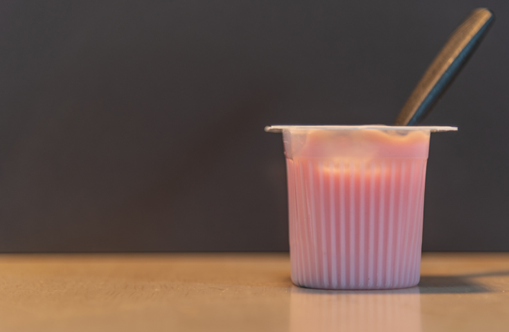 A cup of pink yogurt on a gray background.