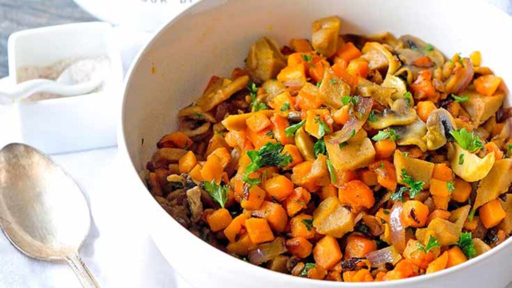 A white bowl filled with Sweet Potato Breakfast Scramble. A spoon lays to the left of the bowl.