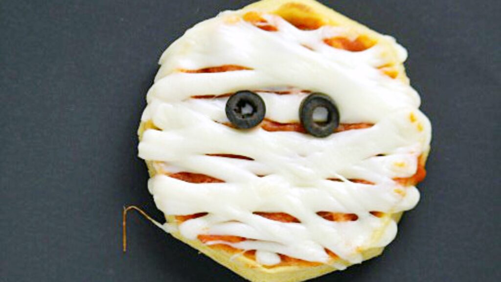 A waffle with olive eyes and cheese placed to look like a mummy.