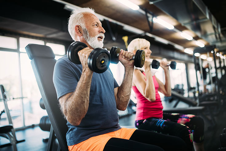 An older couple lifting weights in a gym.