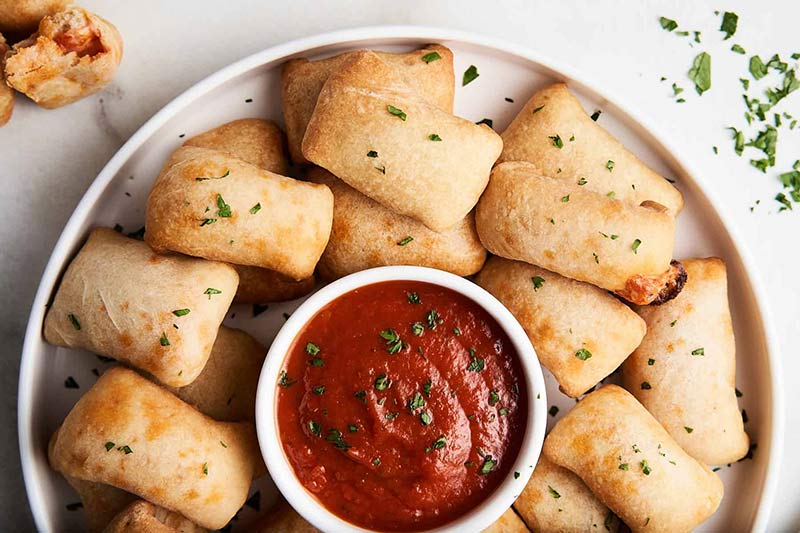 An overhead view of a platter of air fryer pizza rolls with a small bowl of dip in the middle.