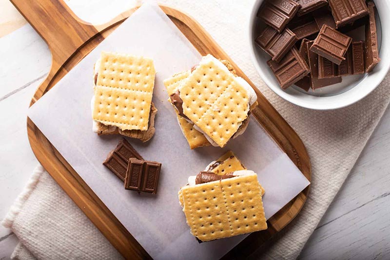 An overhead view of three s'mores on a cutting board.