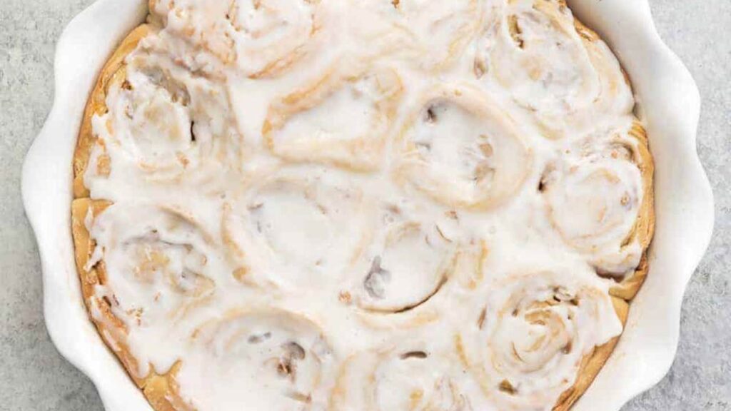 A round baking pan full of apple pie cinnamon rolls frosted with cream cheese frosting.