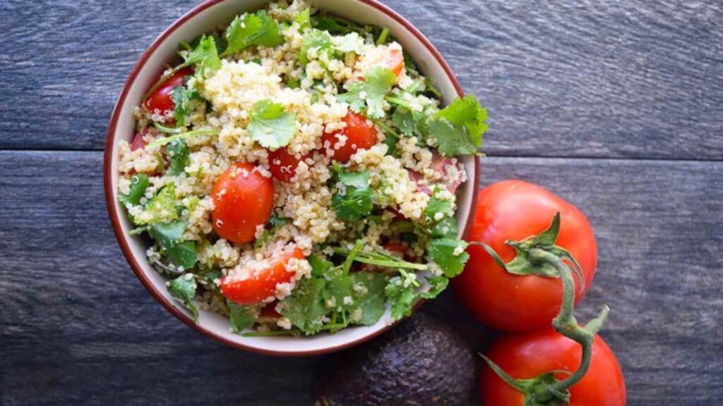 Avocado quinoa salad in a bowl with two whole tomatoes on the vine sitting next to it.