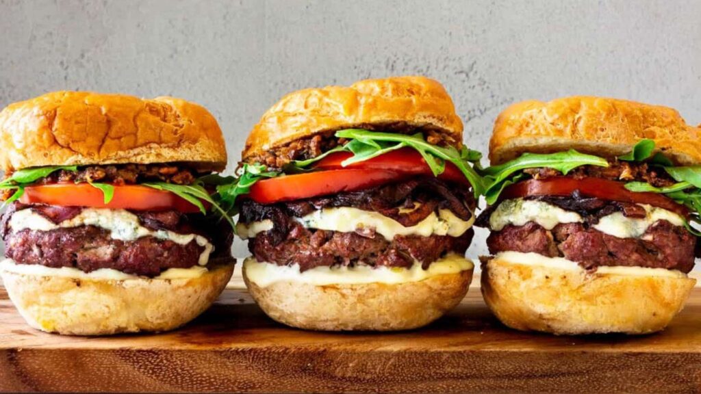 Three burgers lined up on a cutting board.