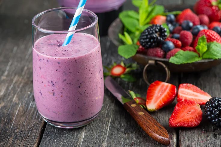 A blueberry smoothie sitting on a table next to a bowl of fresh berries.