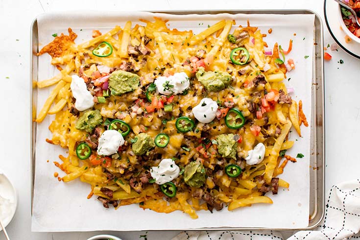 An overhead view of a parchment-lined baking sheet covered in carne asada fries.