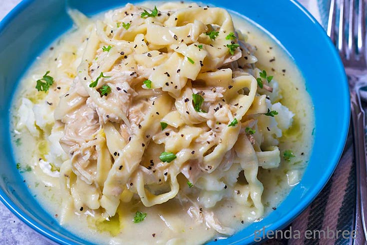A blue bowl filled with Chicken and noodles over mashed potatoes.