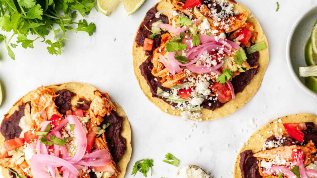 Three chicken tostadas on a white surface.