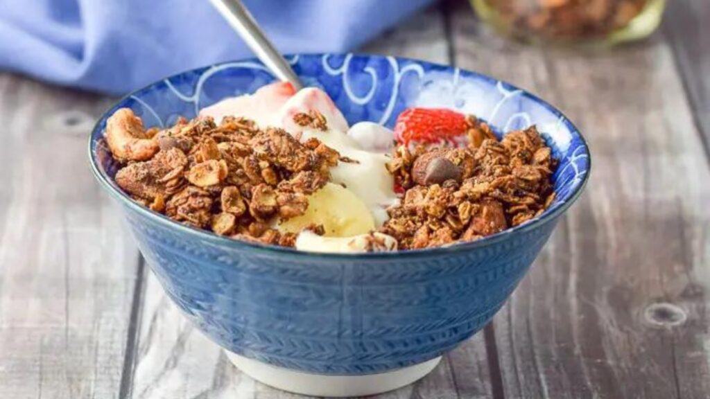 A blue bowl on a wood surface filled with chocolate peanut butter granola.