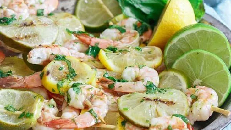 A platter of shrimp on skewers with lemon and lime slices.