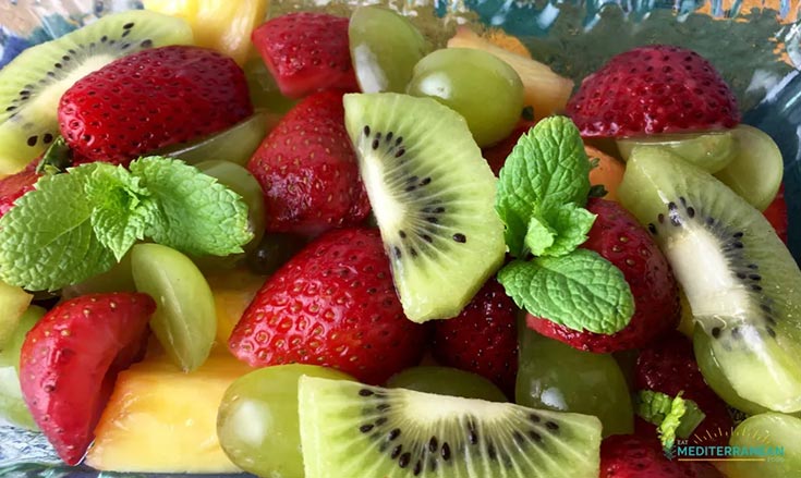 A closeup of a fruit salad with strawberries, grapes, kiwi and melon.