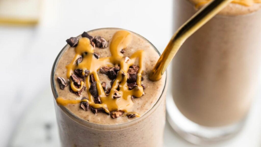 A closeup of a chocolate peanut butter smoothie in a glass with a metal straw.