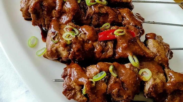 A white platter holding skewers of Indonesian chicken satay.