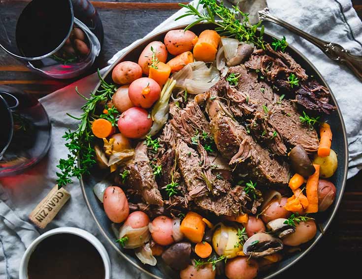 A plate holds slices of venison roast with potatoes and carrots surrounding it.