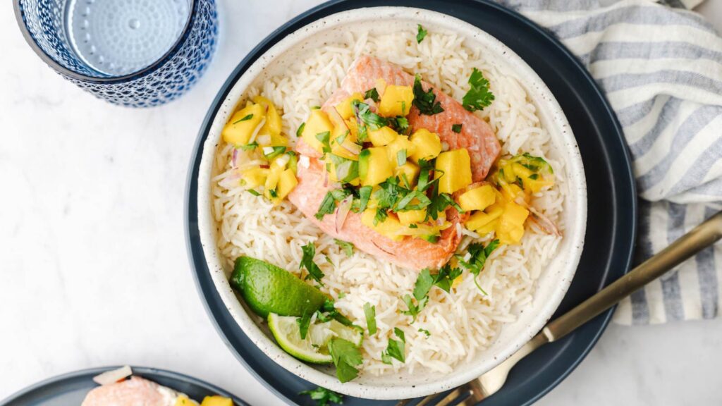 An overhead view of a plate with a bed of rice with a salmon fillet topped with mango salsa.