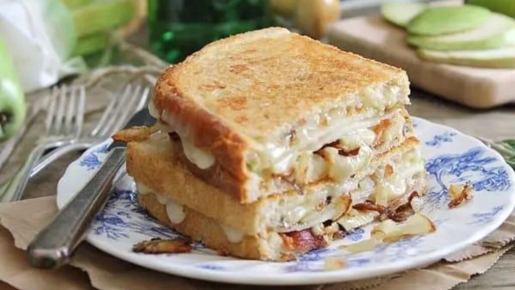 A cut pear and bacon grilled cheese sandwich on a plate.