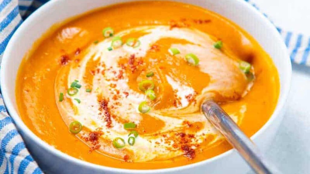 A white bowl filled with Roasted red pepper tomato basil soup.