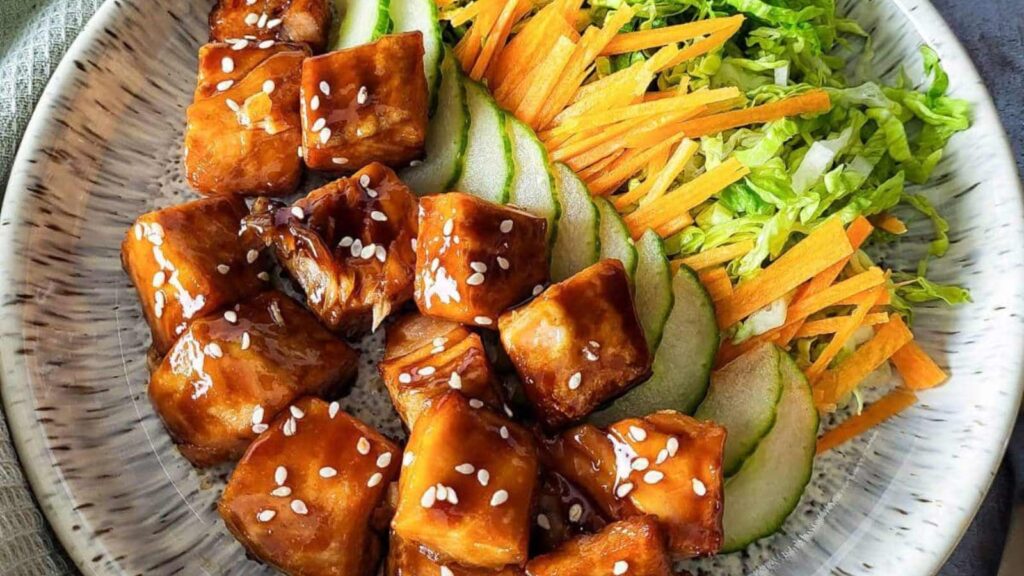 A plate with salmon bits and fresh vegetables next to them.