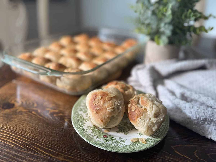 Three Scottish Oatmeal Rolls on a plate with a casserole dish filled with them sitting behind it.