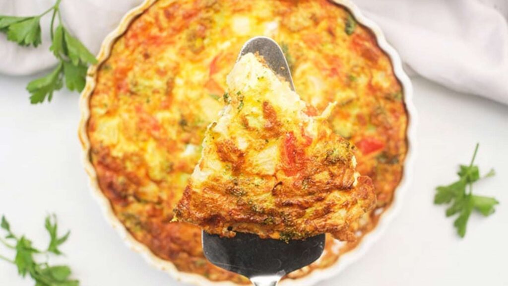 A spatula lifts a slice of Vegetable Breakfast Tart up out of a tart pan.