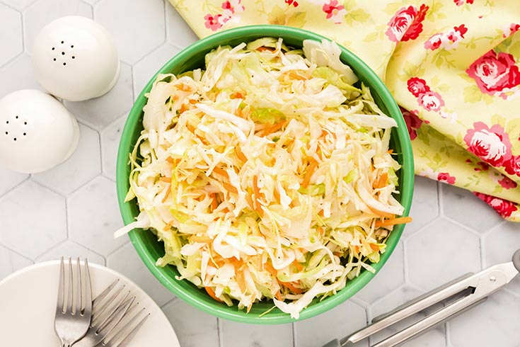 A green bowl filled with coleslaw, sitting on a countertop.