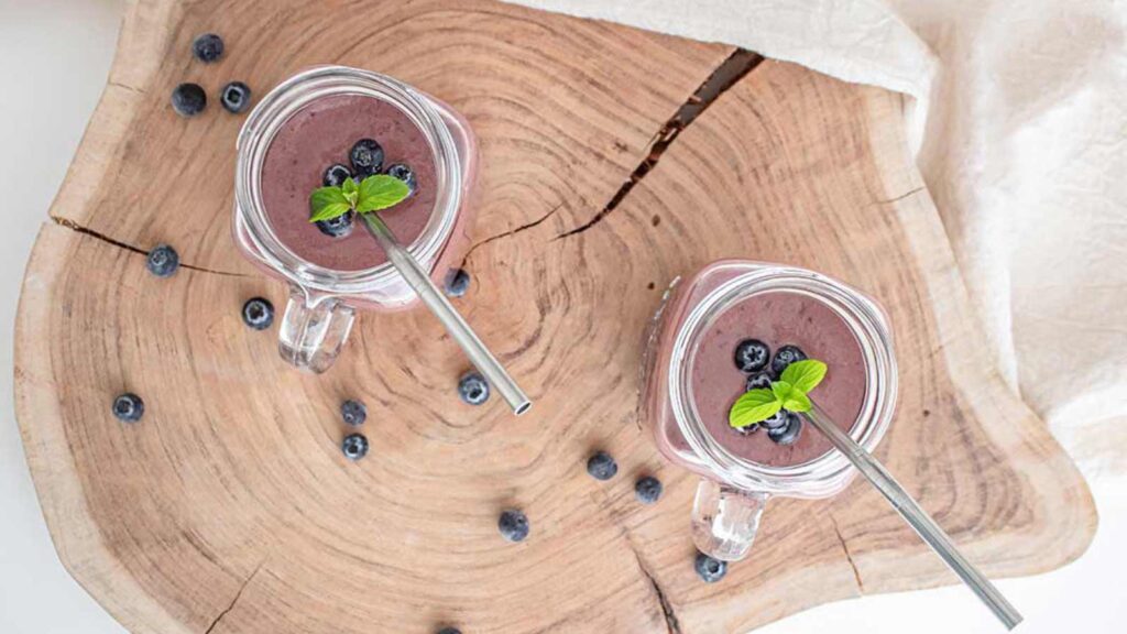 An overhead view looking down into two glass mugs filled with Acai Smoothie and garnished with mint leaves and fresh berries.