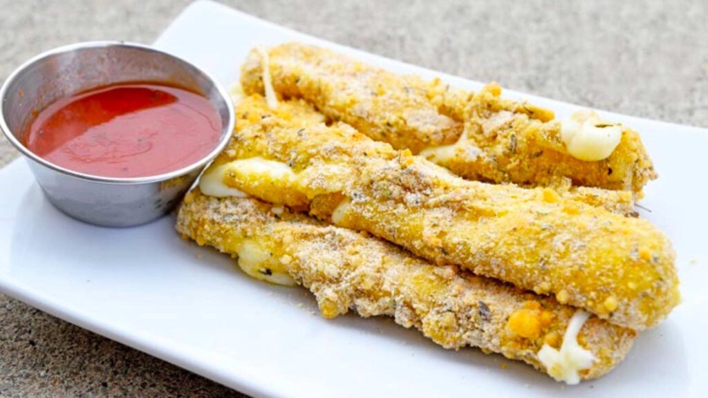 A rectangular white plate holding a small pile of air fryer cheese sticks.