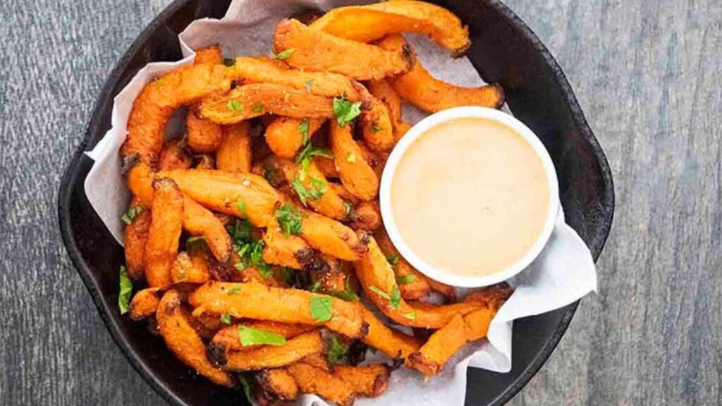 An overhead view of a cast iron skillet filled with sweet potato fries and a small dish of dip.