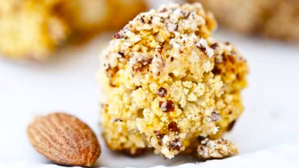 A closeup of an almond crusted roasted cauliflower floret with an almond laying next to it.