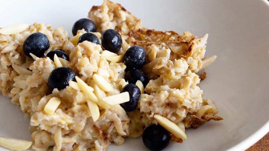 A serving of baked oatmeal with blueberries on top in a white bowl.