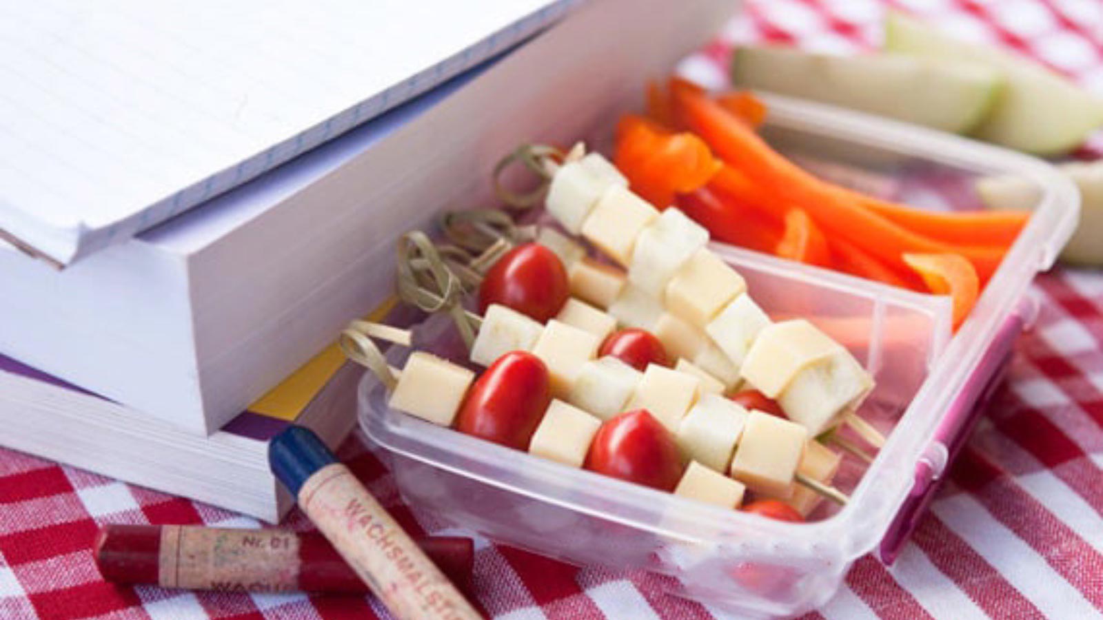 Apple & Gouda Kabobs in a small lunch container on a table next to some books.